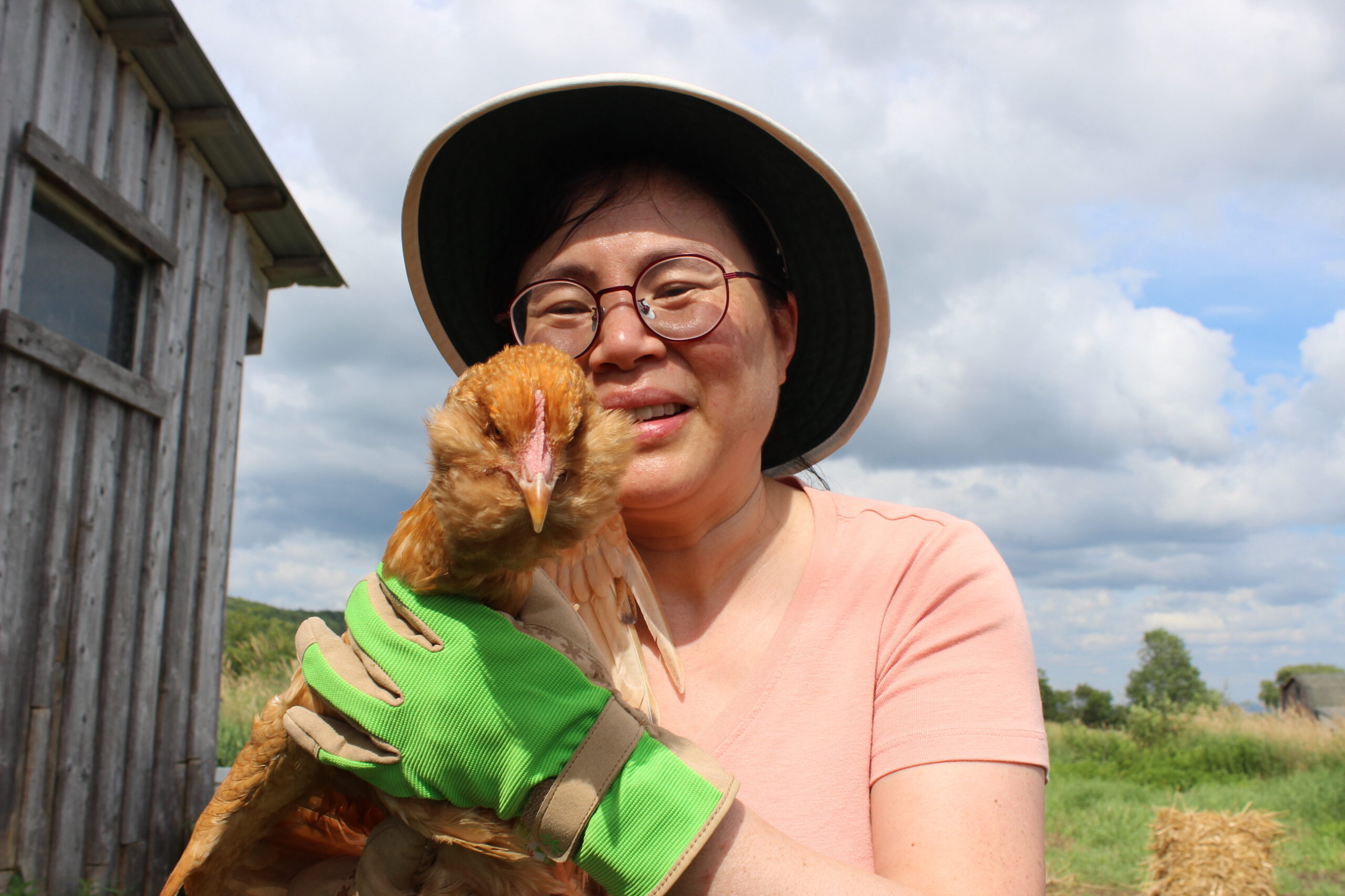 Photograph of an Asian woman wearing a hat and holding a chicken